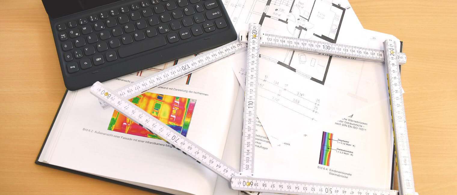 Lehrbuch über Wärmebrücken mit Maßstab in Form eines Hauses und Tablet obenauf