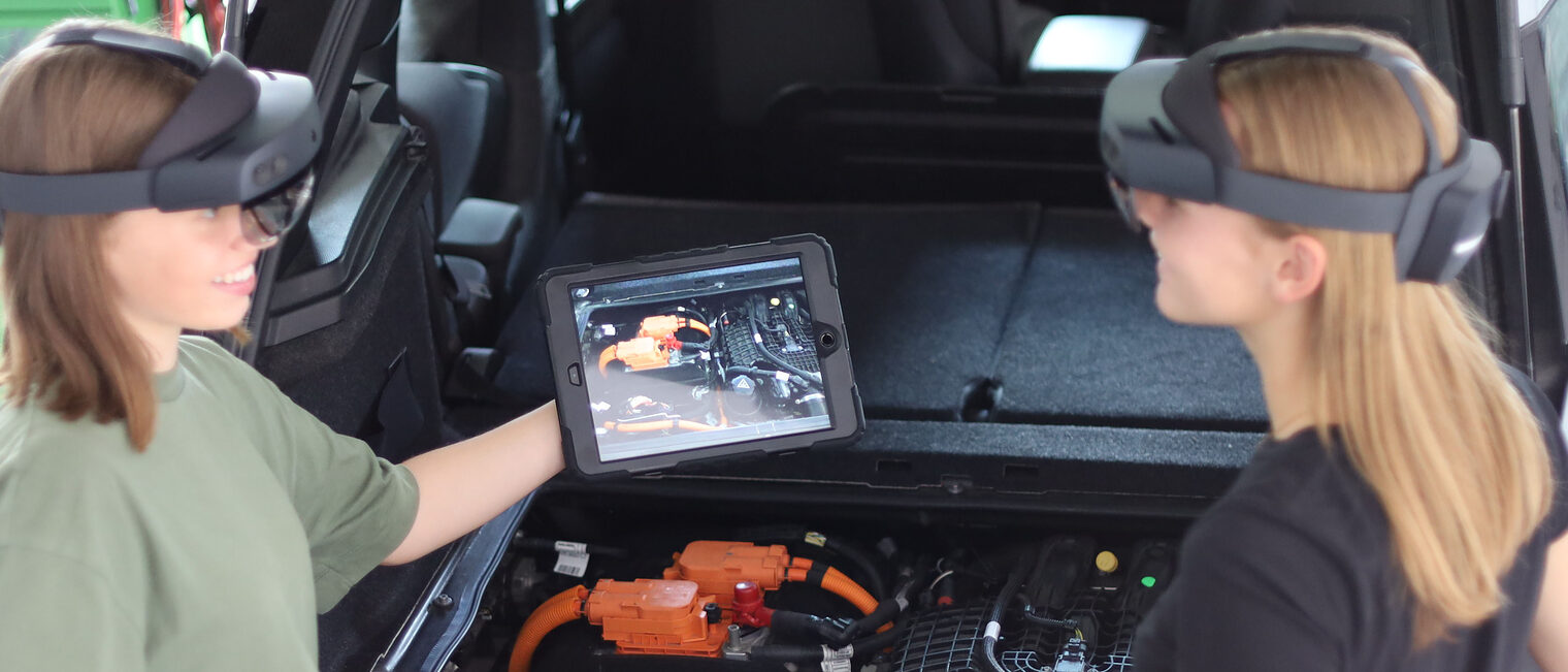 Zwei Mädchen mit Tablet und AR-Brille vor Motorraum