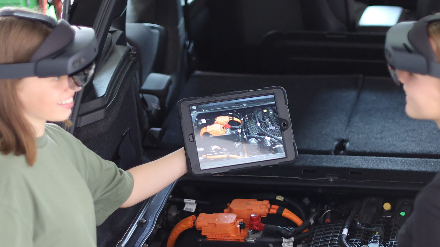 Zwei Mädchen mit Tablet und AR-Brille vor Motorraum