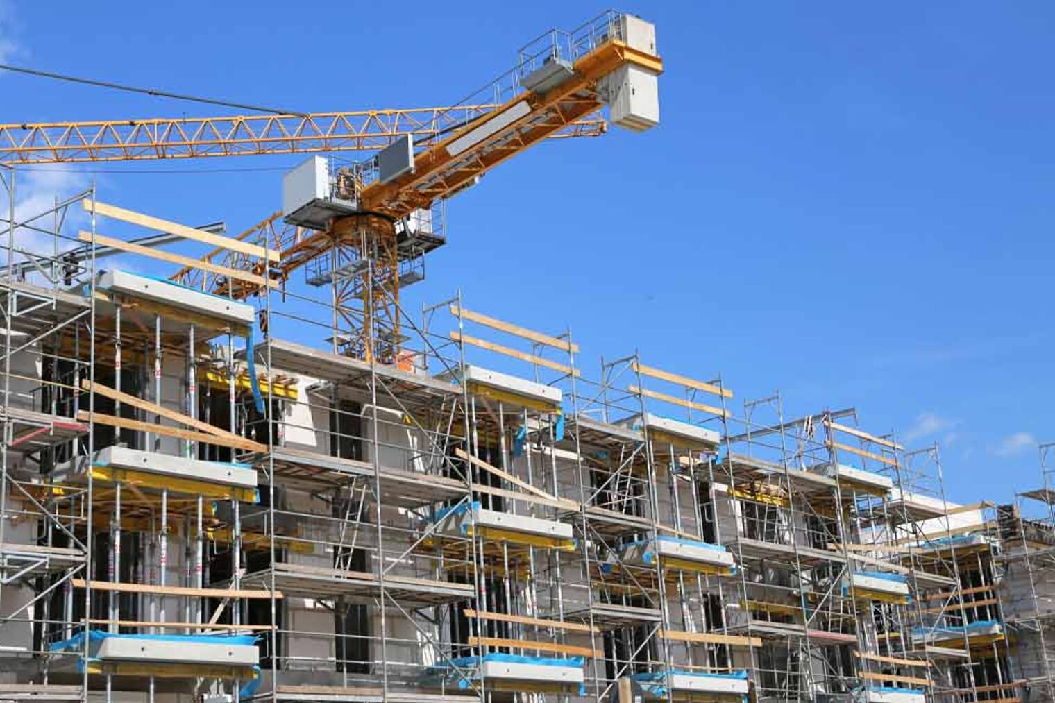 Baustelle | Kurzarbeitergeld Baubranche Mehrfamilienhaus Rohbau mit Gerüst und Baukran dahinter