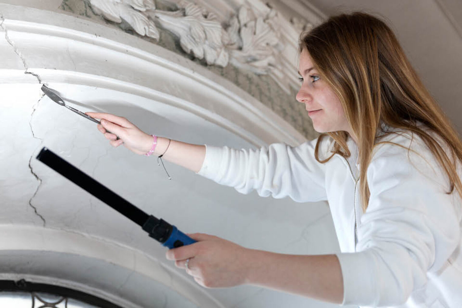 Ausbildung Handwerk Stuckateurin arbeitet an einem Riss in historischer Fassade