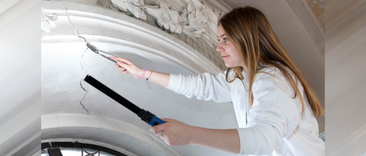 Ausbildung Handwerk Stuckateurin arbeitet an einem Riss in historischer Fassade