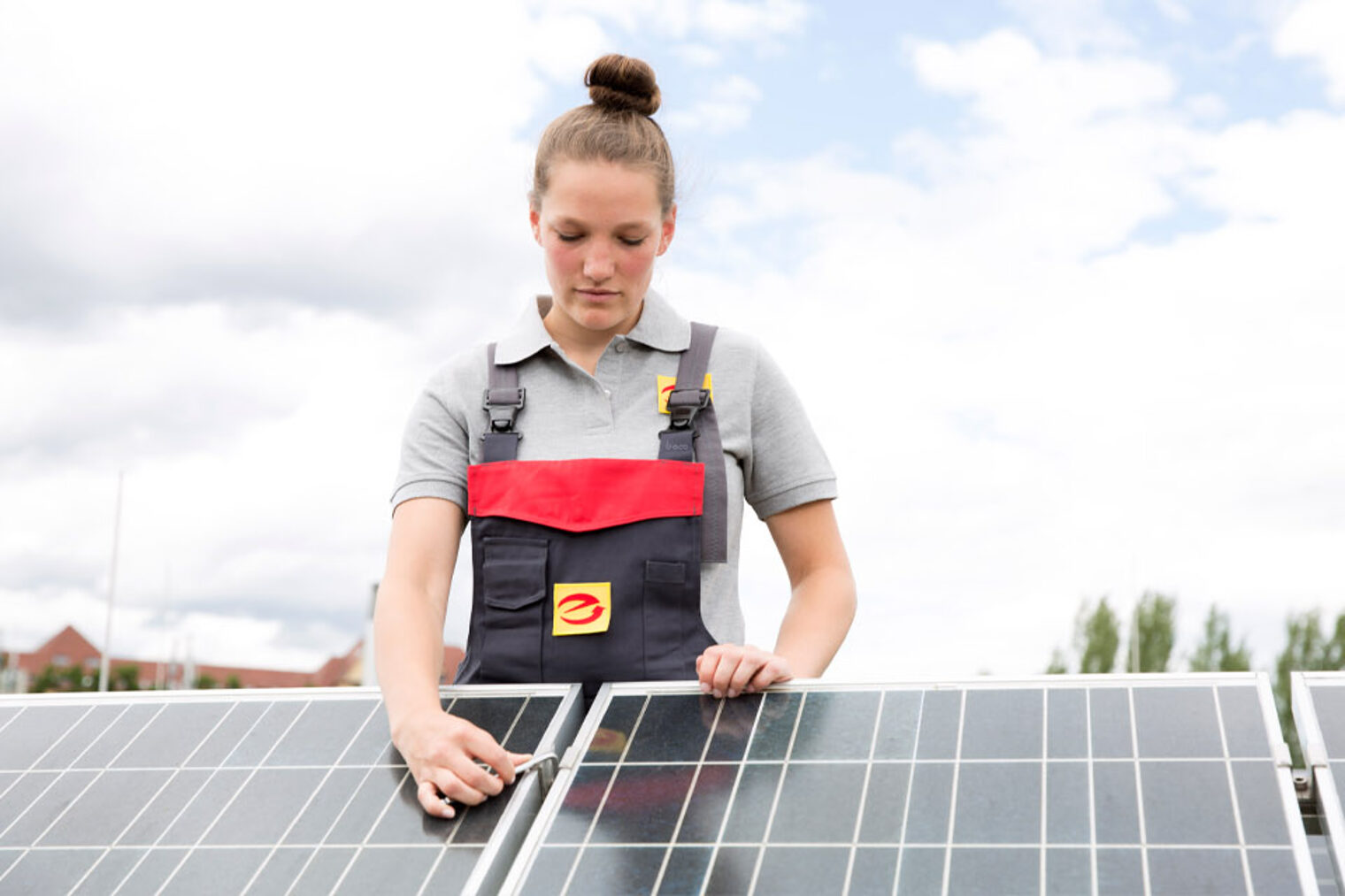 Elektronikerin auf einem Dach, die an PV-Modul schraubt