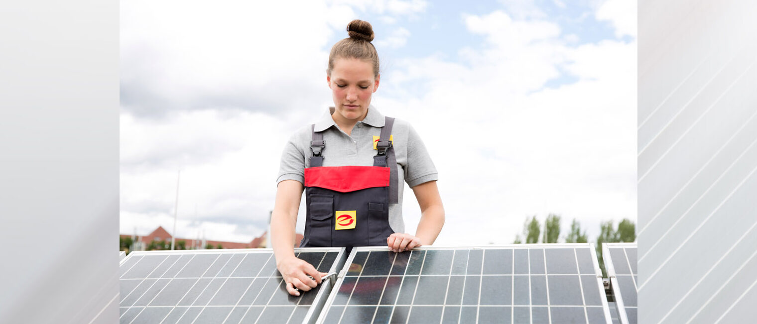 Elektronikerin auf einem Dach, die an PV-Modul schraubt