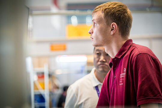 Junger Mann im Seitenprofil, Polohemd dunkelrot mit Aufschrift WorldSkills Germany, Lichtschein von vorne in sein Gesicht
